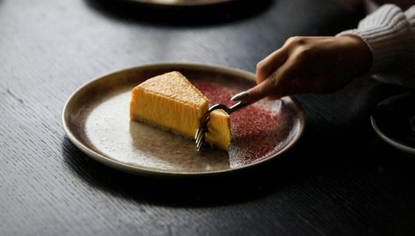 hand cutting the cheesecake on a plate and black wooden table