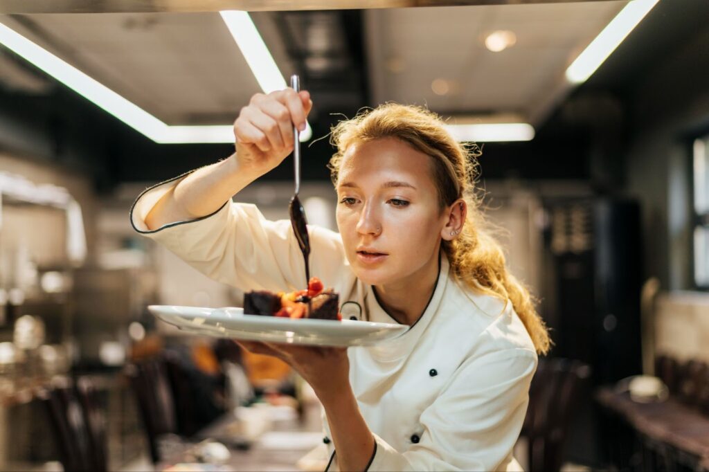 The female chef adds sauce to the dish