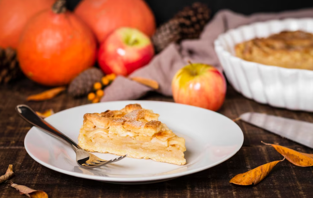 a piece of apple pie, fork on the white plate, leaves, apples, pumpkin on the table